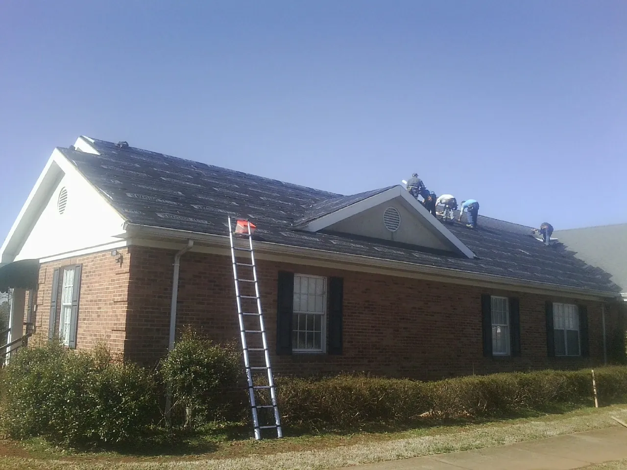 Crew tearing shingles off a brick ranch roof with a ladder set — Emergency Roof Repair work by our crew in Dennis
