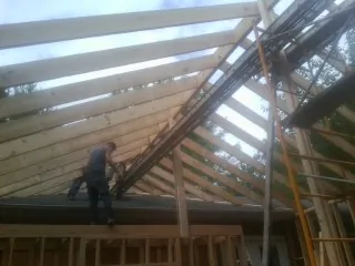 Rafters going up over a new addition with a worker on the wall in Dennis