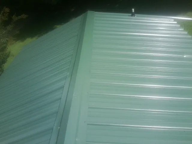 New green metal panels meeting at the ridge of a roof — Flat Roof Repair work by our crew in Dennis
