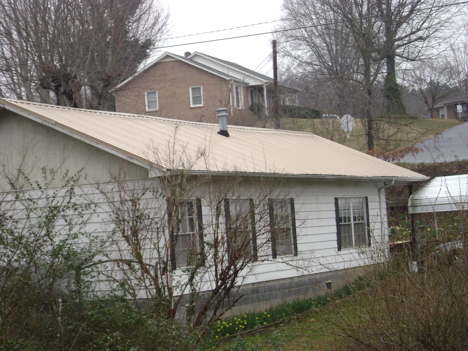 Tan metal roof on a white sided house set into a hillside — Commercial Roofing by Roofing Brothers in Dennis