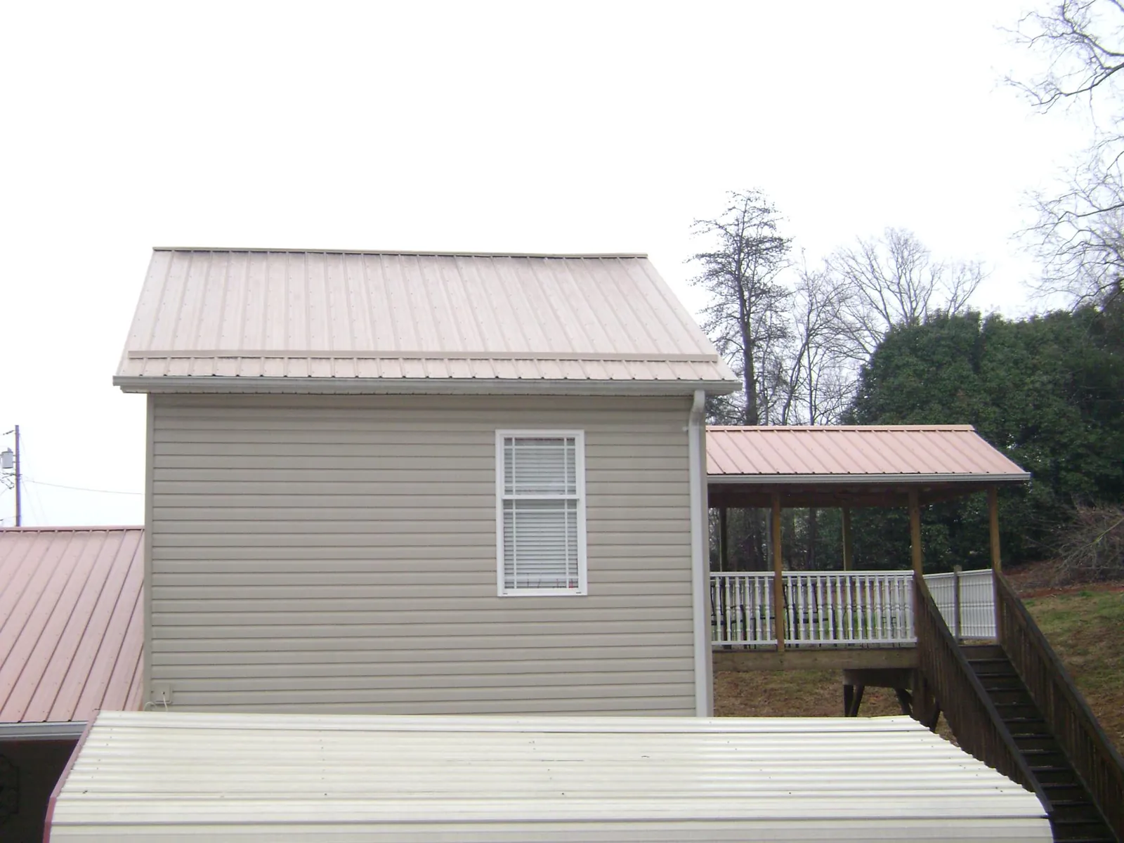 Tan metal roofs on a two story addition and attached porch, from a Roof Replacement job in Dennis